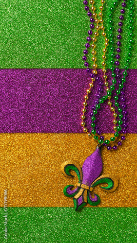 Mardi Gras beads with Fleur de lis, in glittering green, purple, and gold. Sparkling festive background for Mardi Gra in traditional colors.