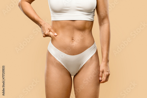 Slim young woman in underwear pinching fat of her waist zone