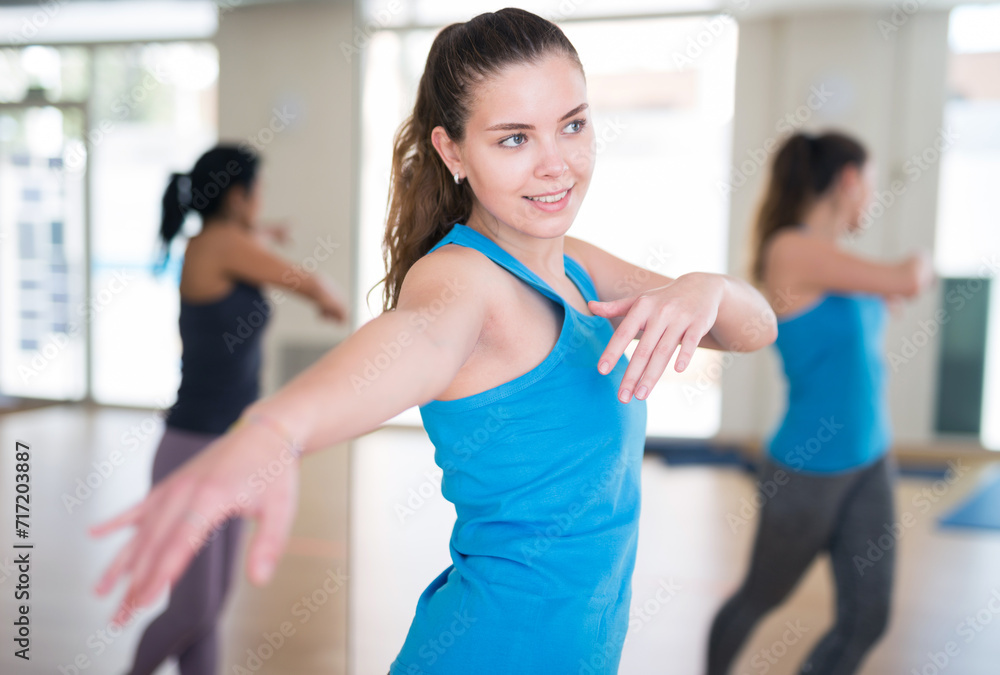 Portrait of smiling dancing girl practicing vigorous swing during group training in dance studio.