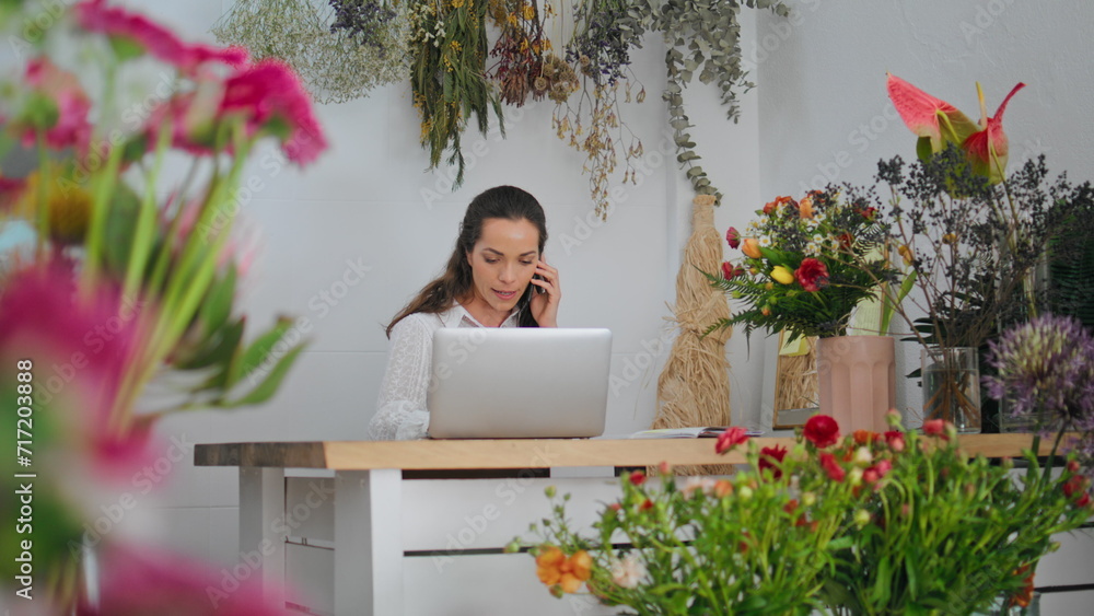 Business florist talk smartphone online in flower shop. Woman work laptop device