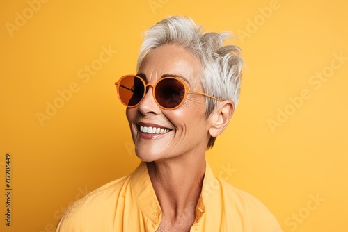 Cheerful mature woman in sunglasses looking at camera over yellow background