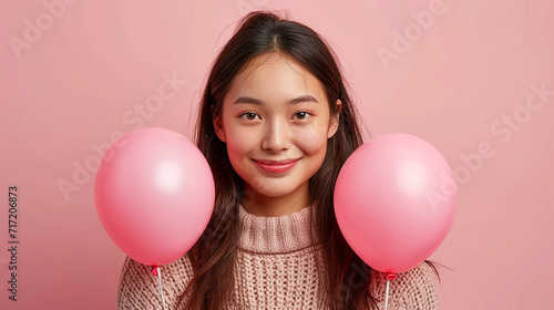 Beautiful asian girl with pink air balloons over pink background. Happy Valentines day. Joyful model smiling and holding ballons in shape of heart.