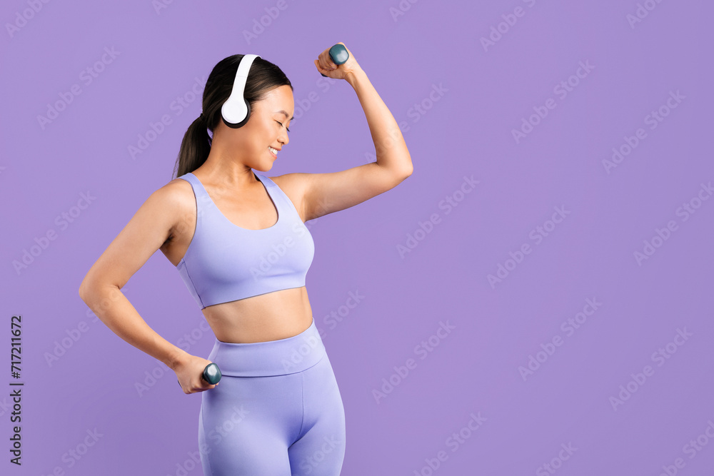 Asian woman in sportswear with headphones flexing muscles with dumbbells Asian woman in sportswear with headphones flexing muscles with dumbbells