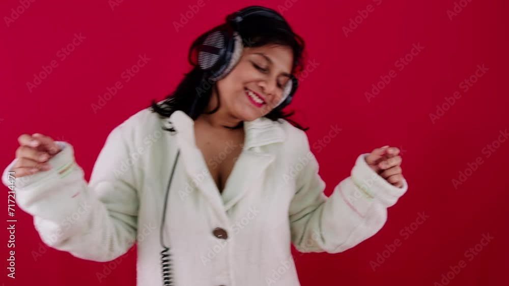 Happy young woman enjoying music with headphones and dancing against a red background Happy young woman enjoying music with headphones and dancing against a red background