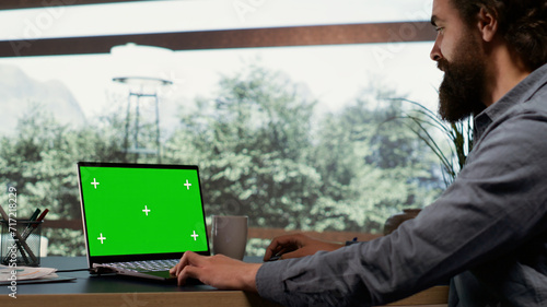 Fotografie Wealthy industrialist unwinds at his elegant property in the mountains, examining greenscreen display on his laptop