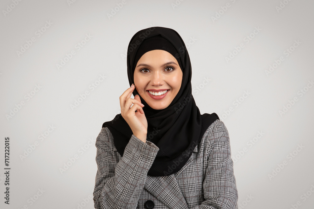 Portrait of muslim businesswoman in hijab smiling at camera, elegantly posing against grey studio background Portrait of muslim businesswoman in hijab smiling at camera, elegantly posing against grey studio background