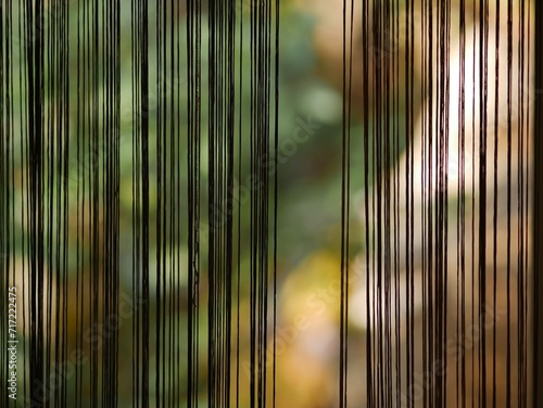 A curtain in the form of vertical threads against a background of green bushes