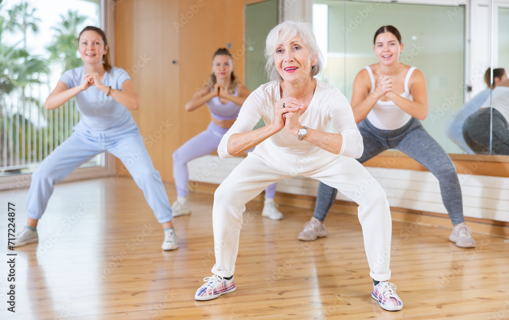 Mature female coach dancing and practicing new movements with group of young women in gym. Dance and wellbeing concept