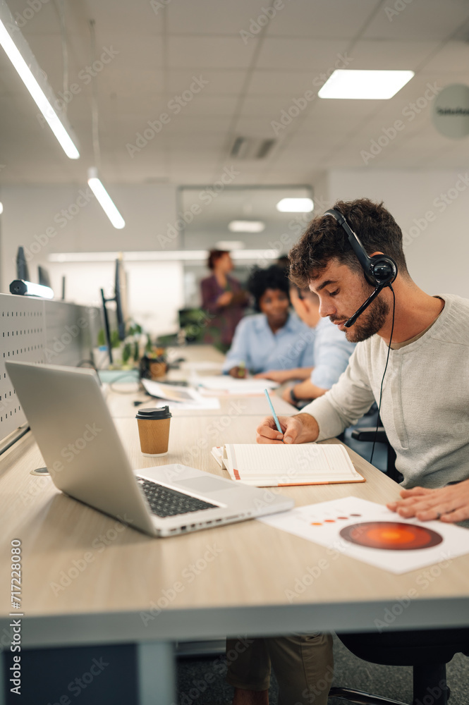 Businessman working in a call center on the line and using headset and a laptop Businessman working in a call center on the line and using headset and a laptop
