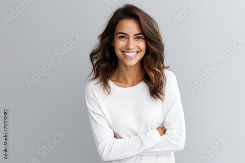 Portrait of a happy young woman with arms crossed against grey background