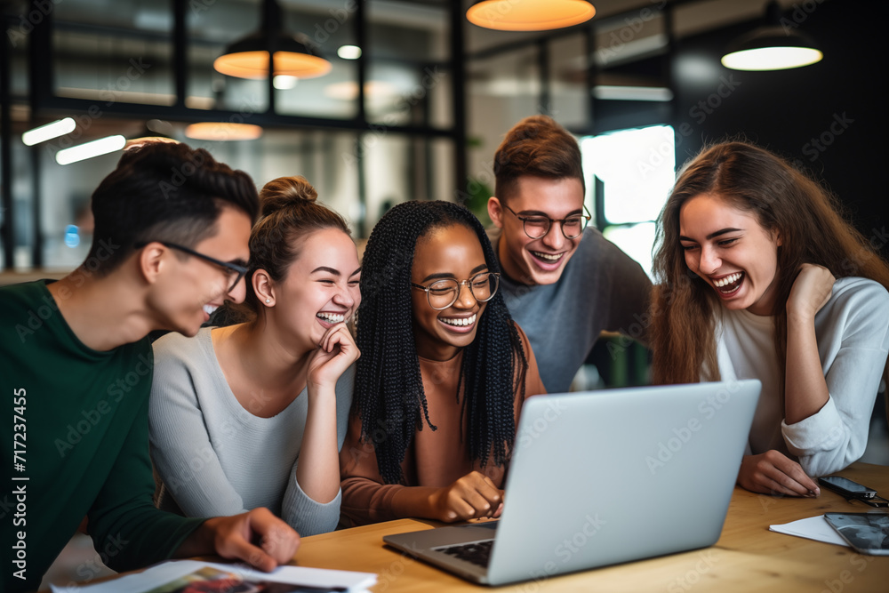 Gruppe lächelnder junger Menschen, die in einem Büro auf einen Laptop schauen, Kollegen mit Spaß und Erfolg im Büro Gruppe lächelnder junger Menschen, die in einem Büro auf einen Laptop schauen, Kollegen mit Spaß und Erfolg im Büro