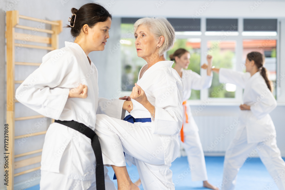 Mature woman in pair exercising karate movements during group training
