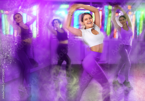 Smiling young girl performing energetic dynamic dance during group training in studio. Colorful toned image with motion blur and vivid light effects