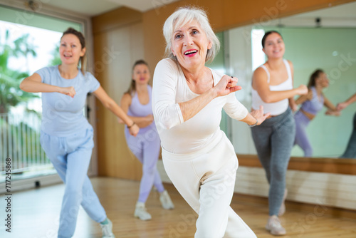 Active aged woman practicing aerobic dance in training hall during fitness dance classes. Women training dance in hall