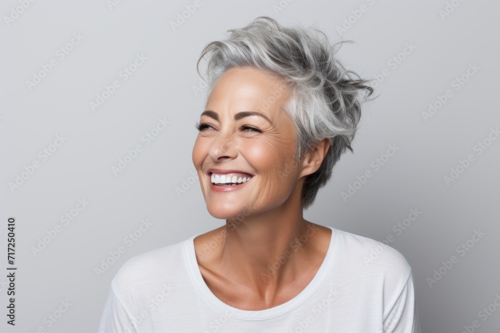 Cheerful mature woman looking away and smiling while standing against grey background Cheerful mature woman looking away and smiling while standing against grey background