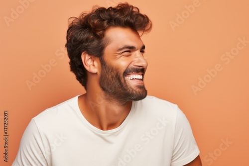 Portrait of a handsome young man laughing and looking away while standing against orange background