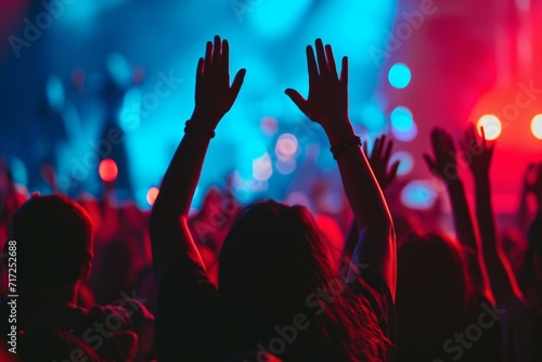 Konzertbesucher heben die Hände in die Luft und tanzen. Livekonzert mit Lightshow und Bühne mit Musikern in der Ferne. Musikkonzert mit feiernden Menschen.  photo