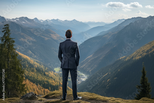 A modern bleisure hiker in a business suit standing triumphantly on a mountaintop, making a call to the office with a breathtaking view of the valley below