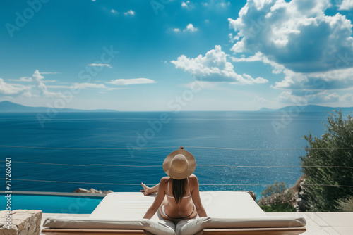 Woman by pool on summer vacation overlooking the ocean in a sunny resort