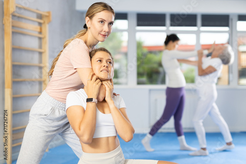 Woman is practicing self-defence moves in pair with her female trainer at gym