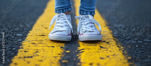 Child in sneakers standing near a yellow line with safety warning, do not cross. photo