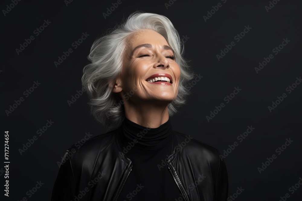 Cheerful mature woman in black leather jacket posing on dark background