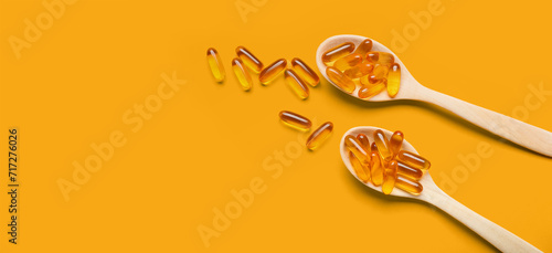 Spoons with fish oil capsules on orange background with space for text photo