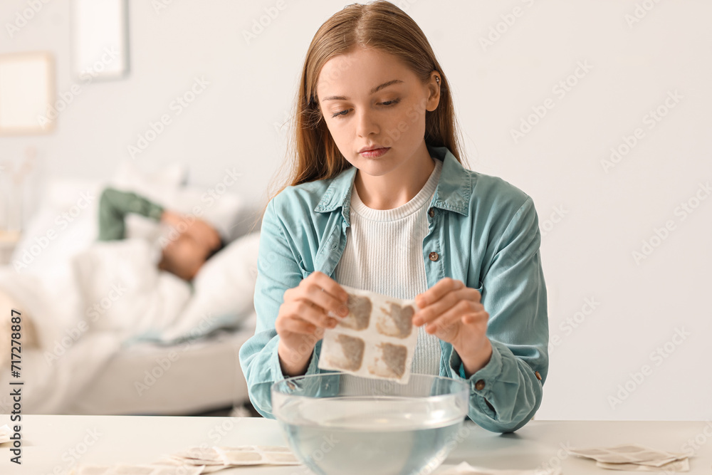 Young woman dipping mustard plaster into bowl of water in bedroom Young woman dipping mustard plaster into bowl of water in bedroom