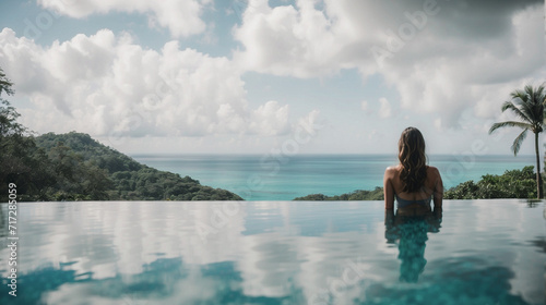 panoramic image Rear view of a woman relaxing serenely in an infinity pool, contemplating a stunning tropical view, embodying tranquility and natural beauty. 