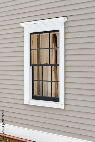 The exterior wall of a grey coloured building is made of narrow horizontal wooden clapboard.  There s a single hung closed block glass window with white crown trim molding and black glass dividers.