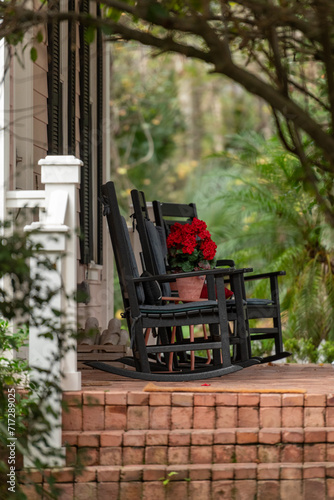Εκτύπωση καμβά A porch or stoop with two wooden rockers, a small table, and a pot of colorful red flowers