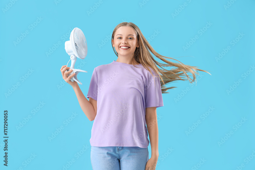 Young woman with electric fan on blue background Young woman with electric fan on blue background