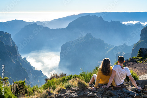 Tourist couple enjoys the picturesque view from the mountain top of a volcanic island on a sunny summer day. Pico do Arieiro, Madeira Island, Portugal, Europe.