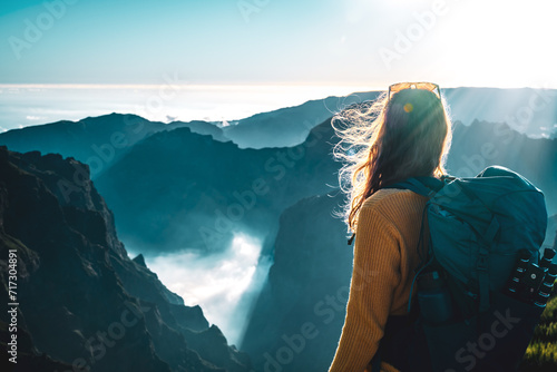 Female backpacker tourist looking at a deep, cloud-covered valley and enjoying the breathtaking view of the volcanic mountain landscape. Pico do Arieiro, Madeira Island, Portugal, Europe. photo