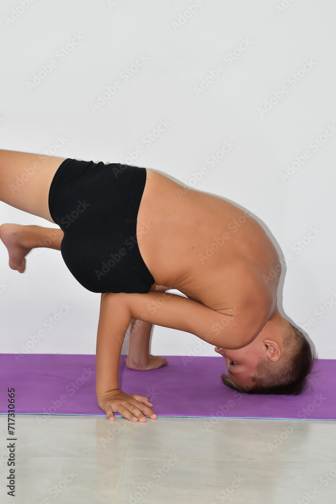 A boy in black shorts on a mat in a yoga pose on his head. A boy in black shorts on a mat in a yoga pose on his head.