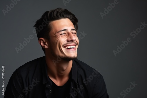 Portrait of a young handsome man laughing against a dark background.