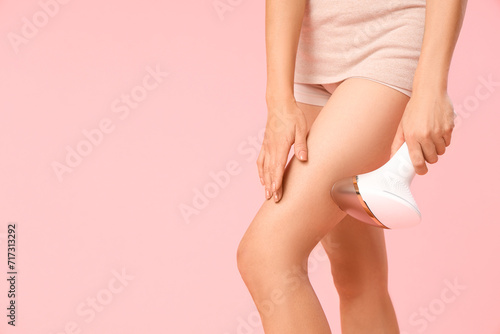 Young woman using photoepilator on her legs against pink background