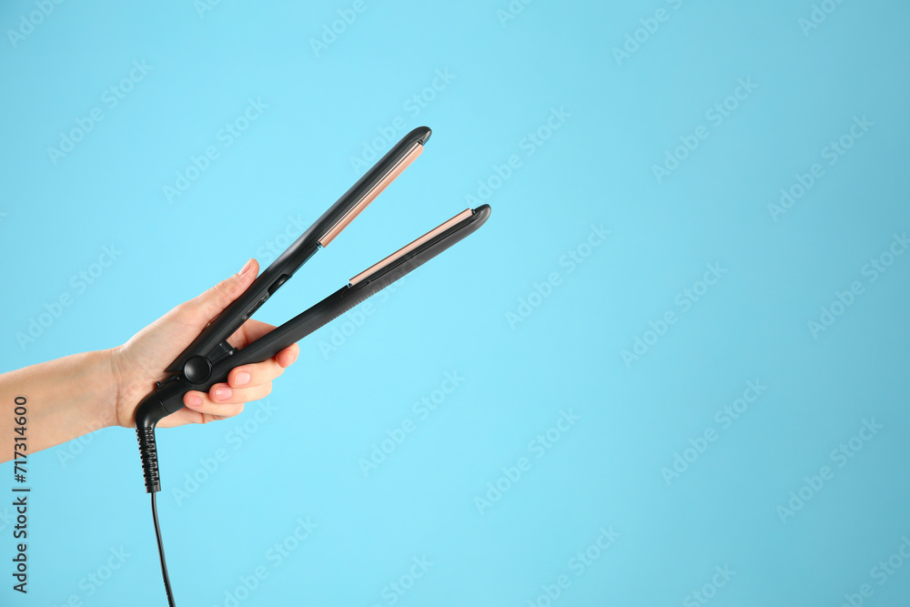 Woman holding corrugated hair iron on light blue background, closeup Woman holding corrugated hair iron on light blue background, closeup