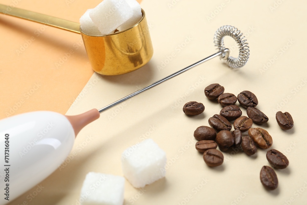 Milk frother wand, coffee beans and sugar cubes on color background, closeup