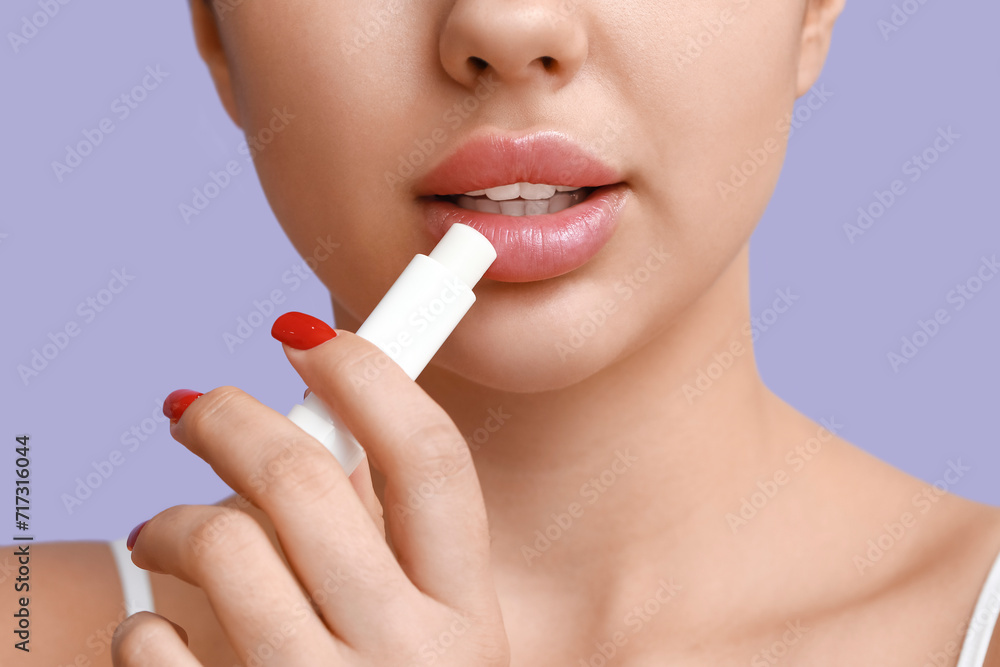 Beautiful young woman applying lip balm on lilac background, closeup Beautiful young woman applying lip balm on lilac background, closeup