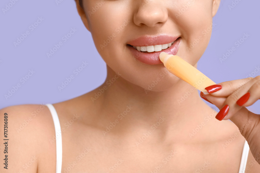 Young woman applying lip balm on lilac background, closeup Young woman applying lip balm on lilac background, closeup