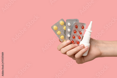 Female hand holding pills in blister packs and nasal spray on pink background photo
