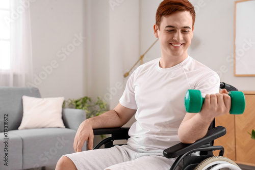 Sporty young man in wheelchair training with dumbbell at home