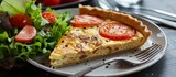 Savory quiche containing homemade crust, caramelized onion, and fresh tomato slices, accompanied by a side of salad.