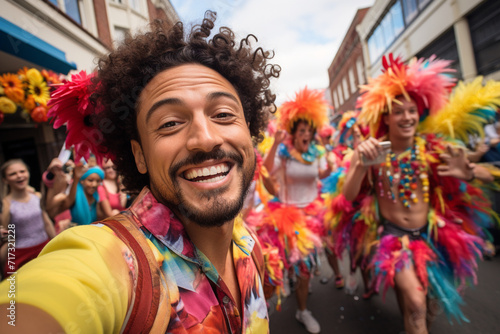 A guy takes a selfie during a vibrant street parade, surrounded by colorful floats, costumes, and lively festivities, capturing the energy of the moment.