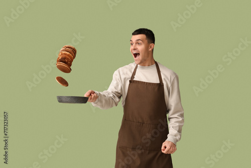 Fotografi Young man frying tasty pancakes on green background