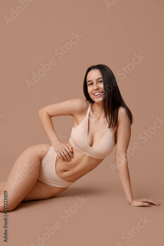 Beautiful young woman in underwear sitting on beige background