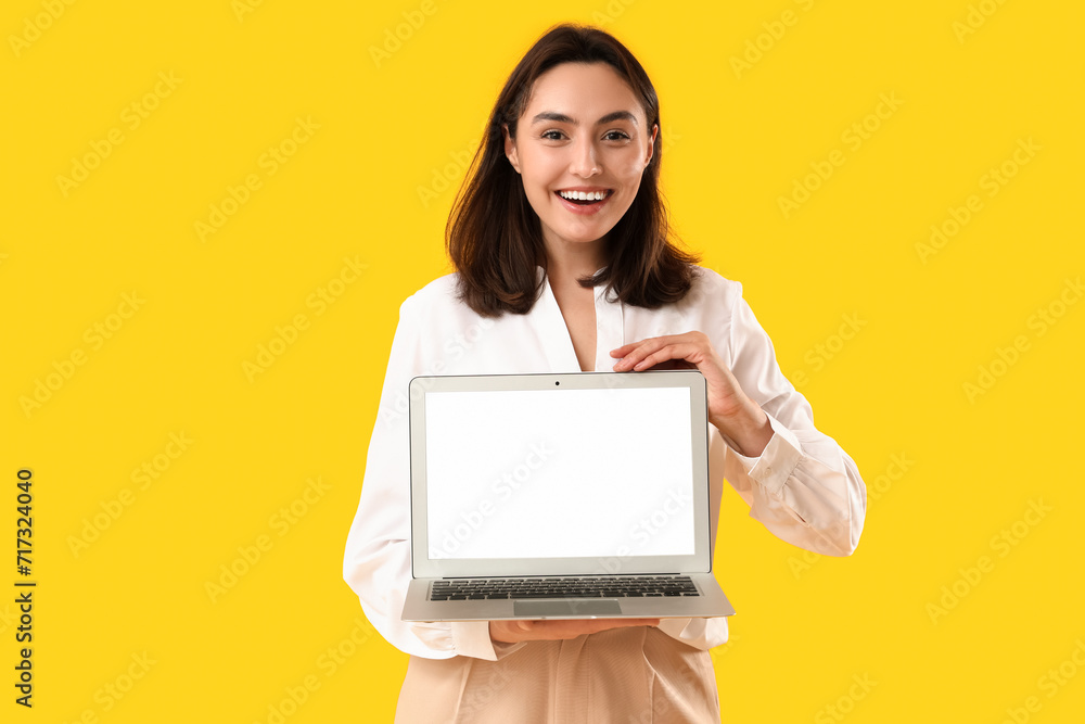 Pretty young woman holding laptop with blank screen on yellow background Pretty young woman holding laptop with blank screen on yellow background