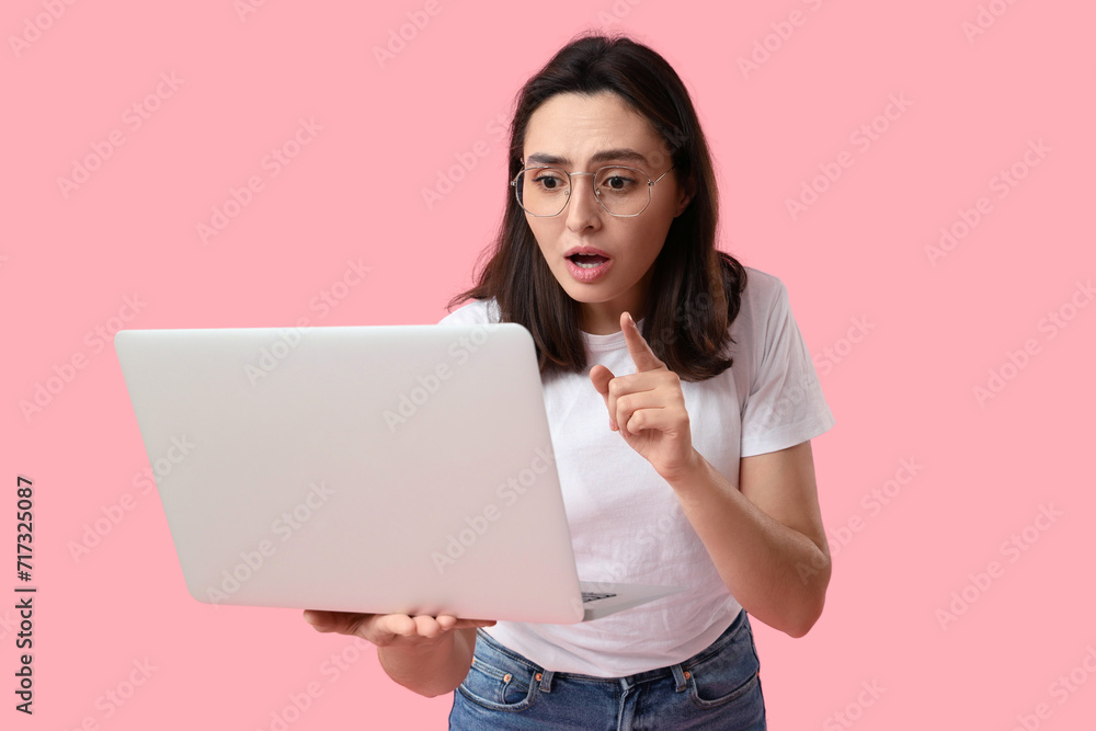 Confused young woman with laptop on pink background Confused young woman with laptop on pink background