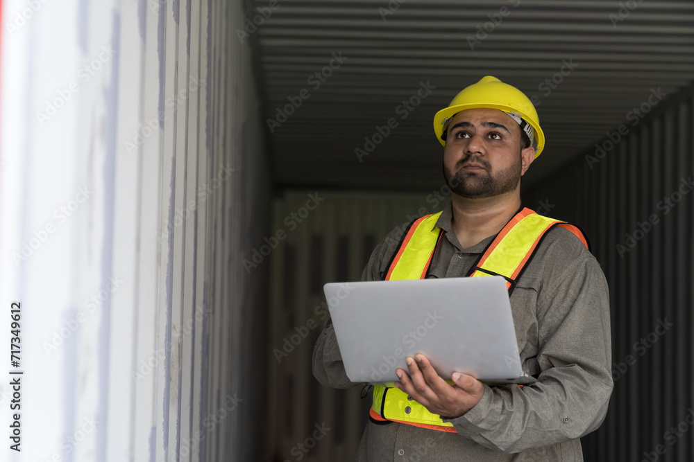 Male container yard worker working and checking into the container boxes before loading at commercial dock site. Male people worker inspecting container boxes from cargo freight ship Male container yard worker working and checking into the container boxes before loading at commercial dock site. Male people worker inspecting container boxes from cargo freight ship